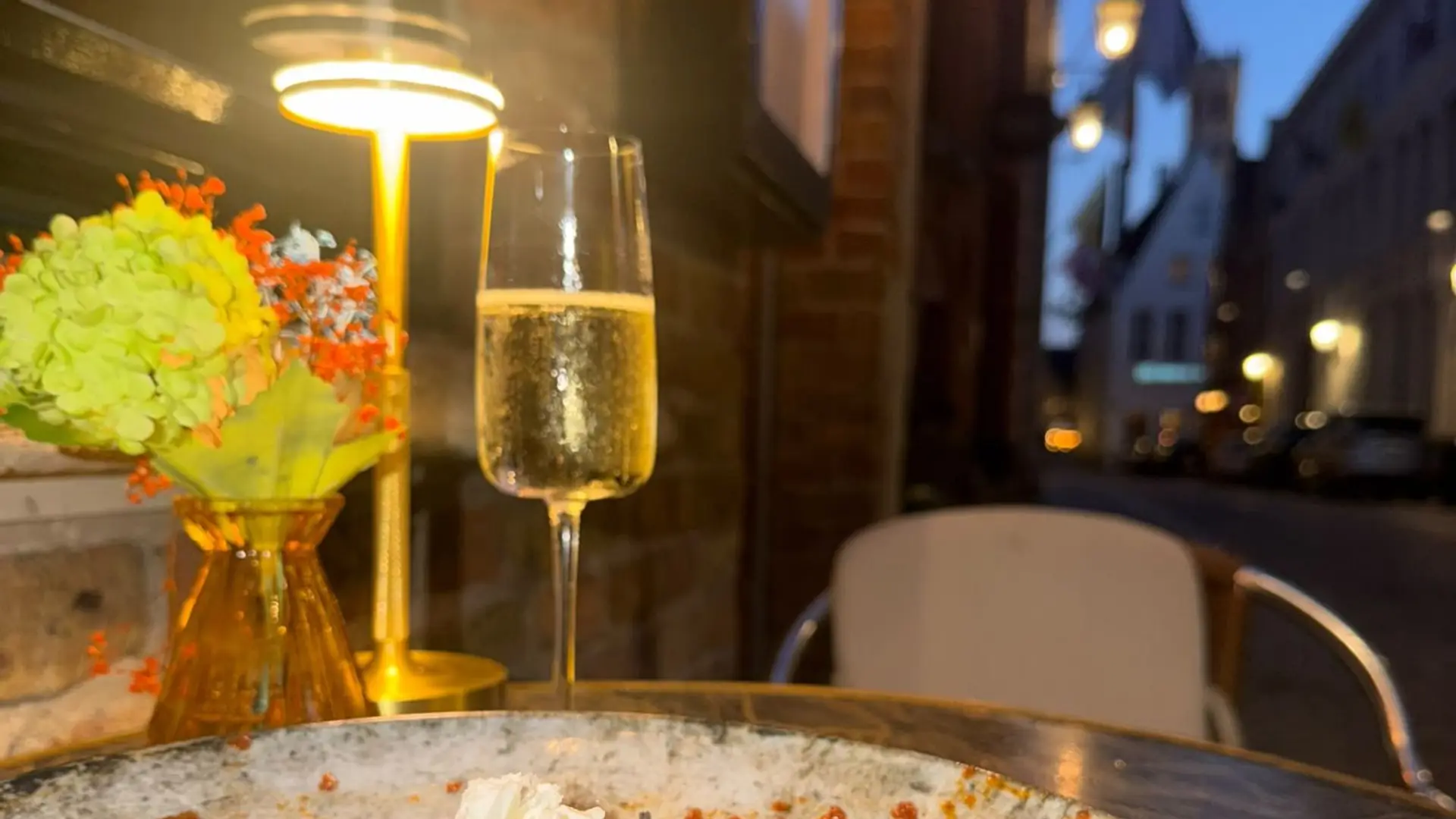 Risotto en een glas bubbels op het terras, met de Brugse straat in de avond