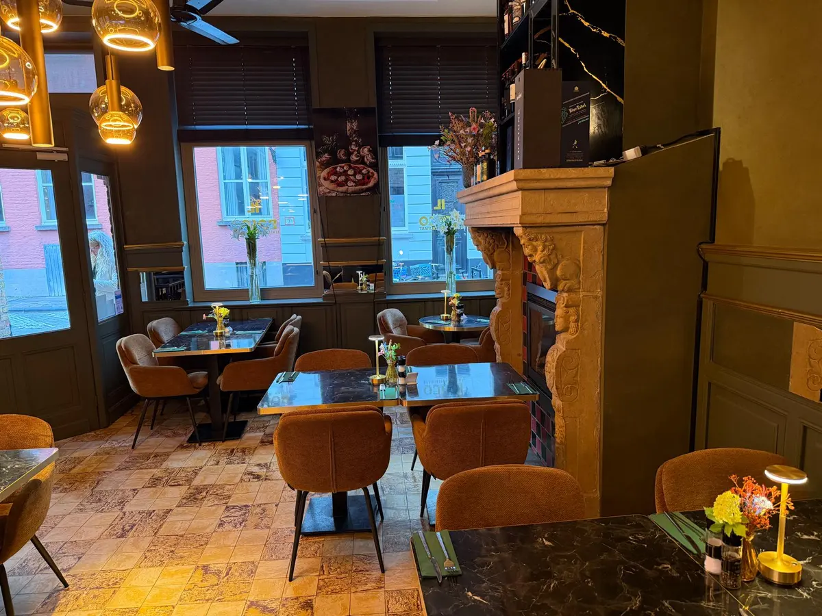 Tafels bij de stenen schouw onder gouden hanglampen